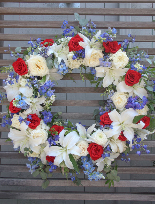 A round funeral wreath with red, white and blue flowers.
