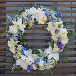 A round funeral wreath with blue and white flowers.