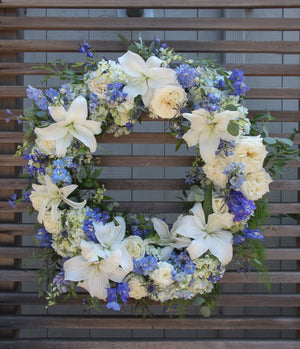 A round funeral wreath with blue and white flowers.