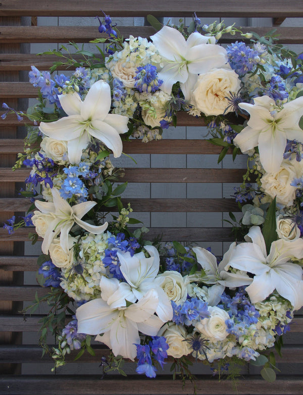 A round funeral wreath with blue and white flowers.