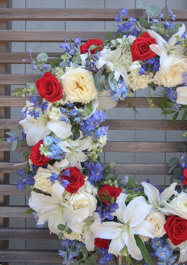A round funeral wreath with red, white and blue flowers for a Veteran or Military Person.