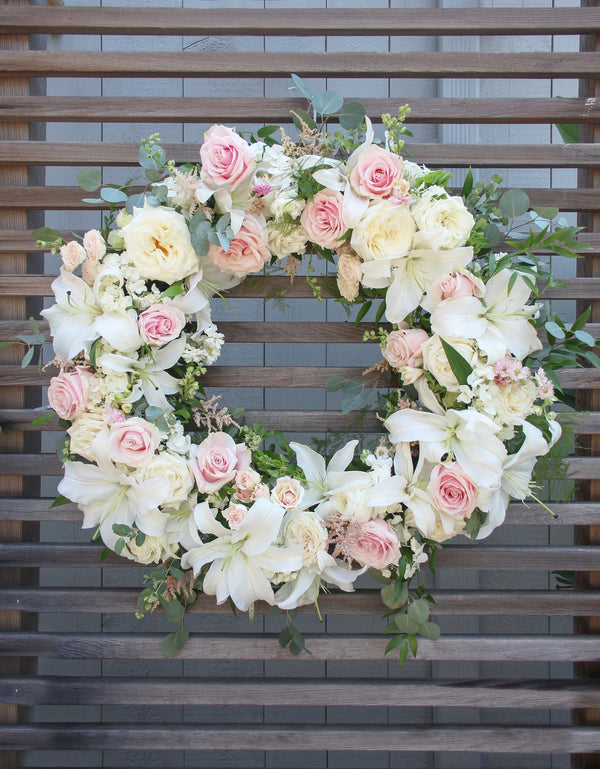A round funeral wreath with white and pale pink flowers