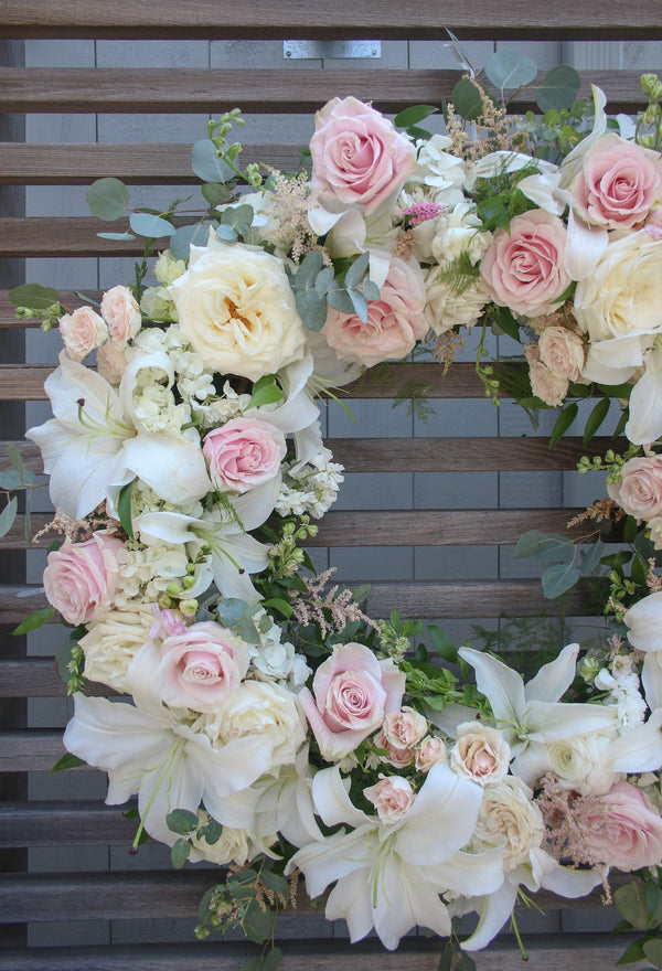 A round funeral wreath with white and pale pink flowers.