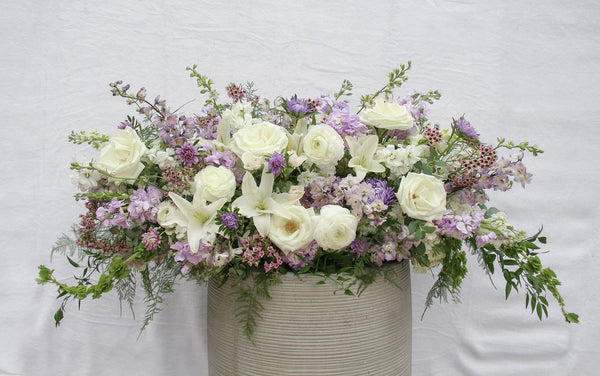 A photo of a Full Casket Cover made with white and pale purple flowers.