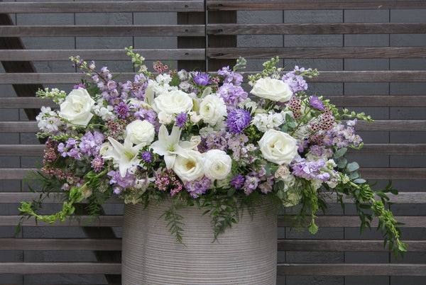 A photo of a Full Casket Cover made with white and pale purple flowers.