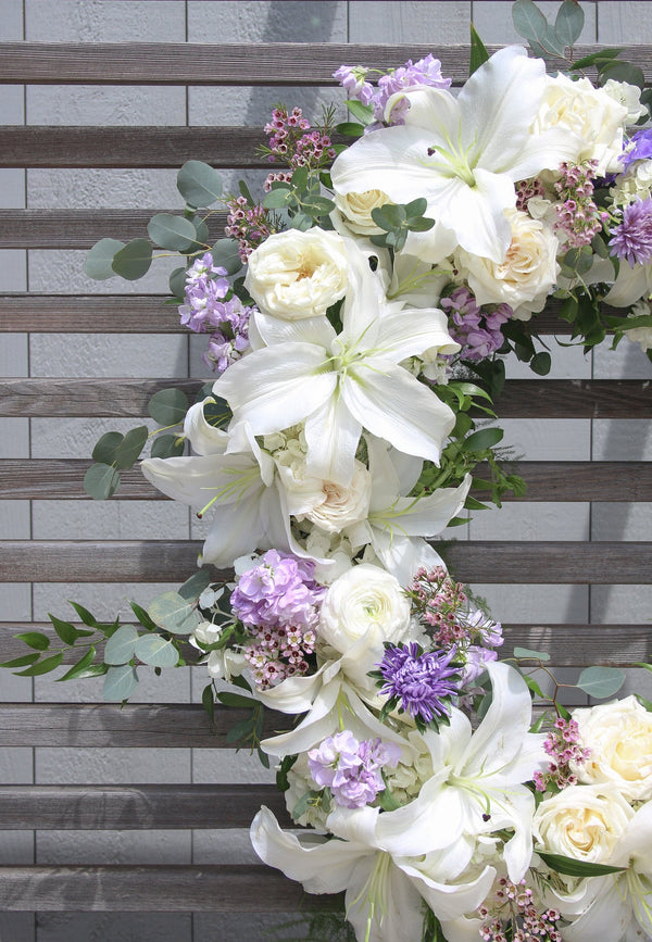 A round funeral wreath with white and pale purple flowers.