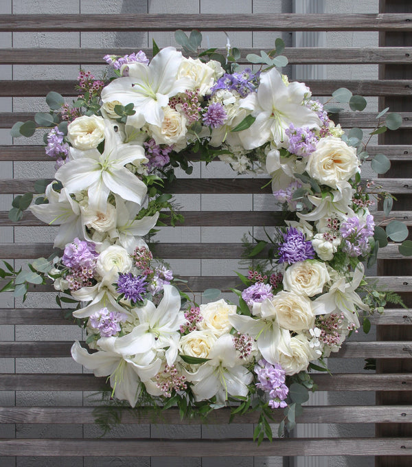 A round funeral wreath with white and pale purple flowers.